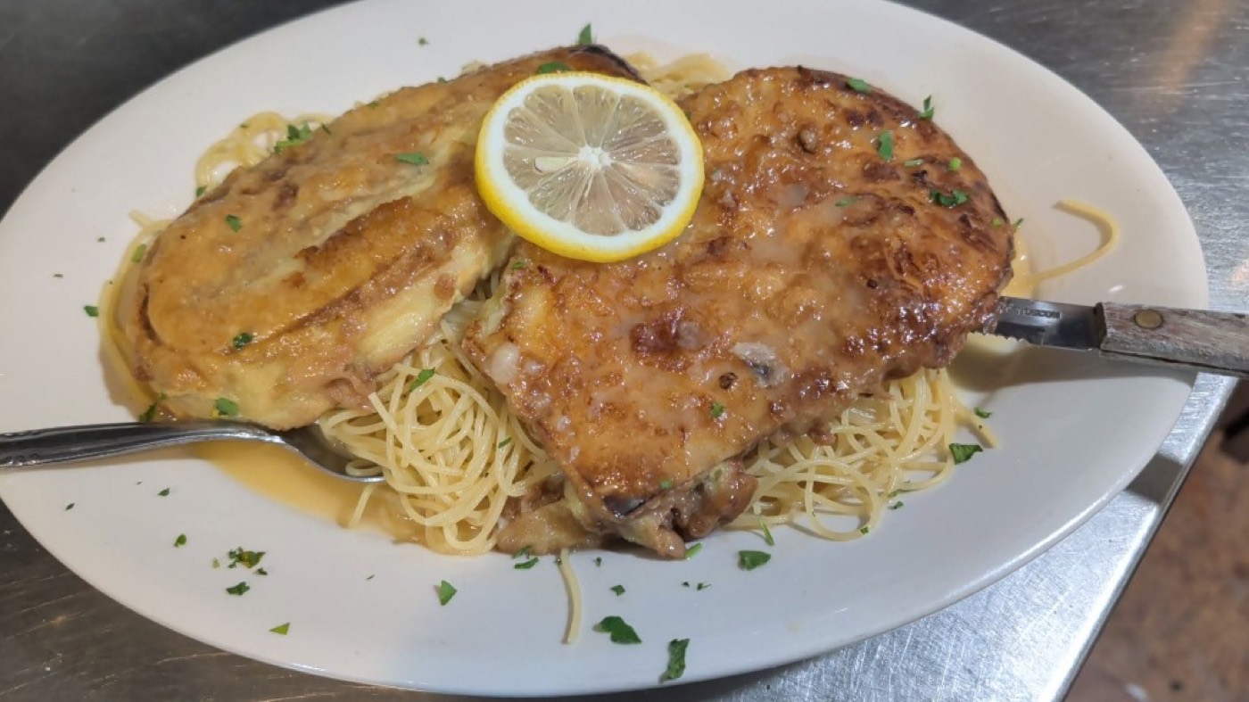 Chicken francese in a lemon butter sauce over spaghetti, with a lemon wheel.